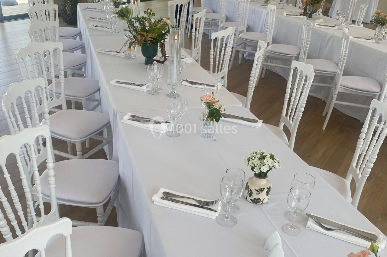 Salle de réception avec tables dressées, nappes blanches, chaises assorties et décorations florales.
