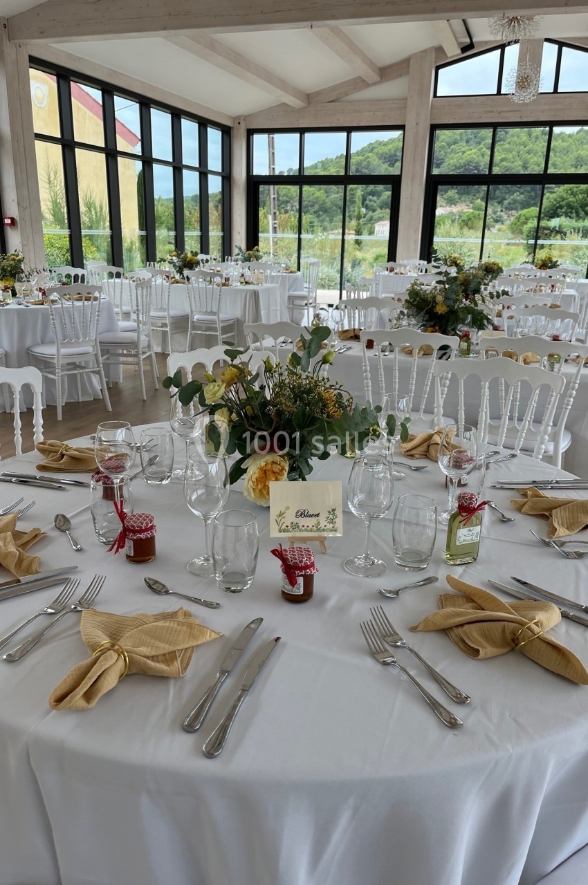 Salle de réception lumineuse avec tables rondes dressées, décorées de fleurs et de nappes blanches.