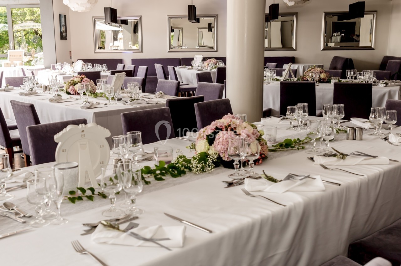 Salle de réception élégamment décorée avec des tables dressées, nappes blanches, fleurs et vaisselle raffinée.