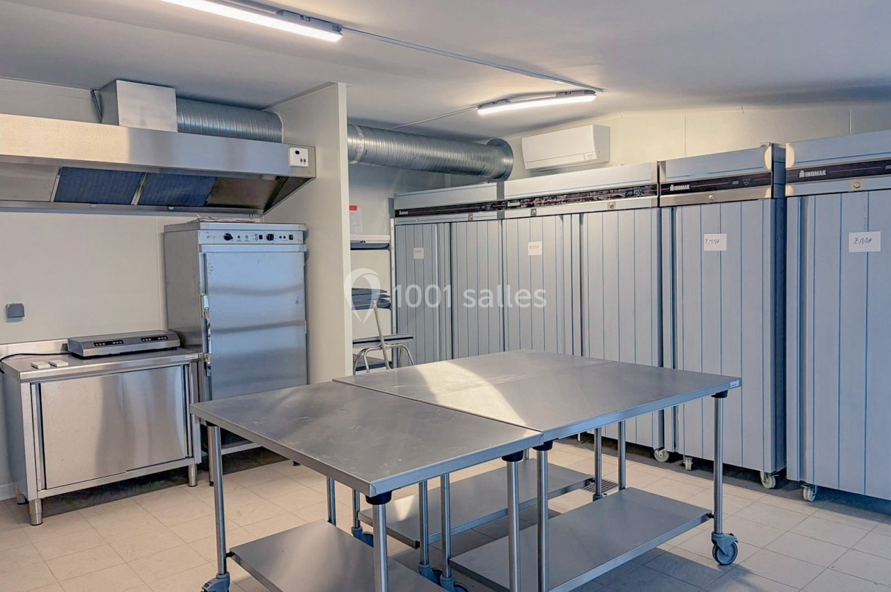 Cuisine professionnelle équipée avec tables en inox, armoires réfrigérées et hotte d'extraction dans un espace lumineux.