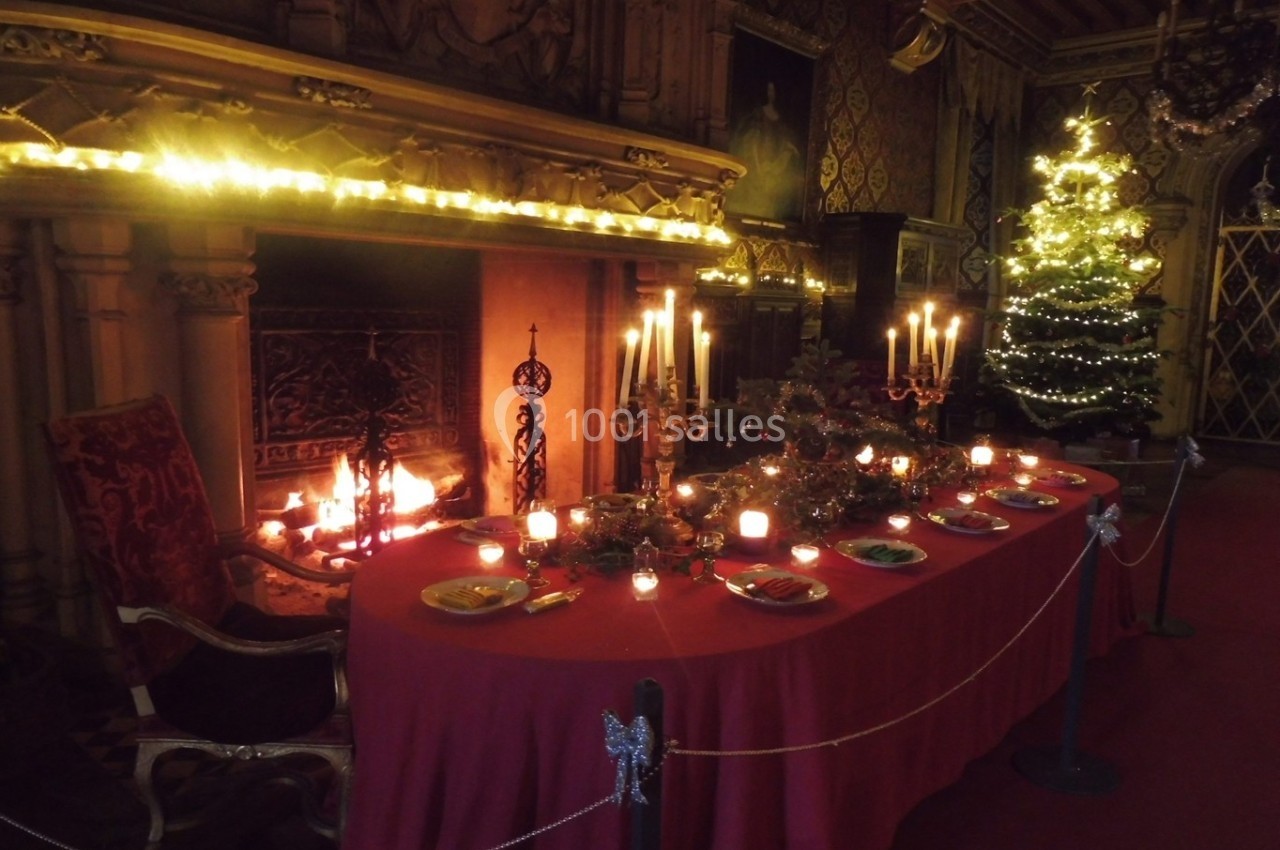 Table décorée pour un dîner festif dans une pièce chaleureuse avec cheminée allumée et sapin illuminé.