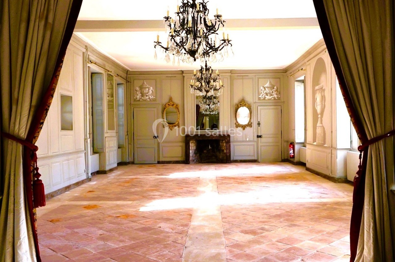 Salle lumineuse avec sol en carreaux de terre cuite, murs ornés de moulures, miroirs et lustres suspendus.