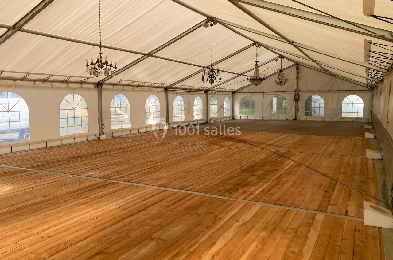 Intérieur d'une grande tente avec un sol en bois, des lustres suspendus et des fenêtres en arc sur les côtés.