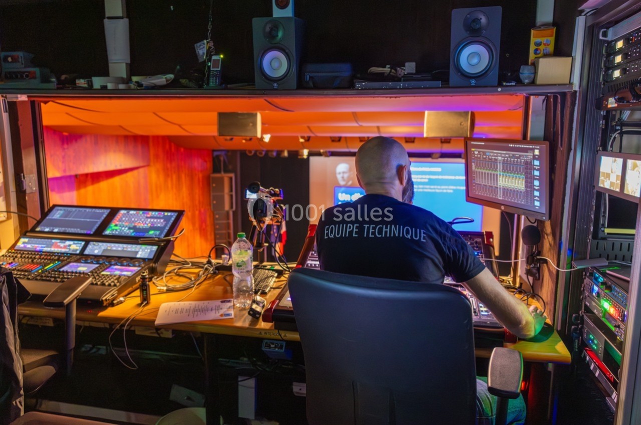 Technicien dans une régie audiovisuelle supervisant des équipements pour un événement en direct sur scène.