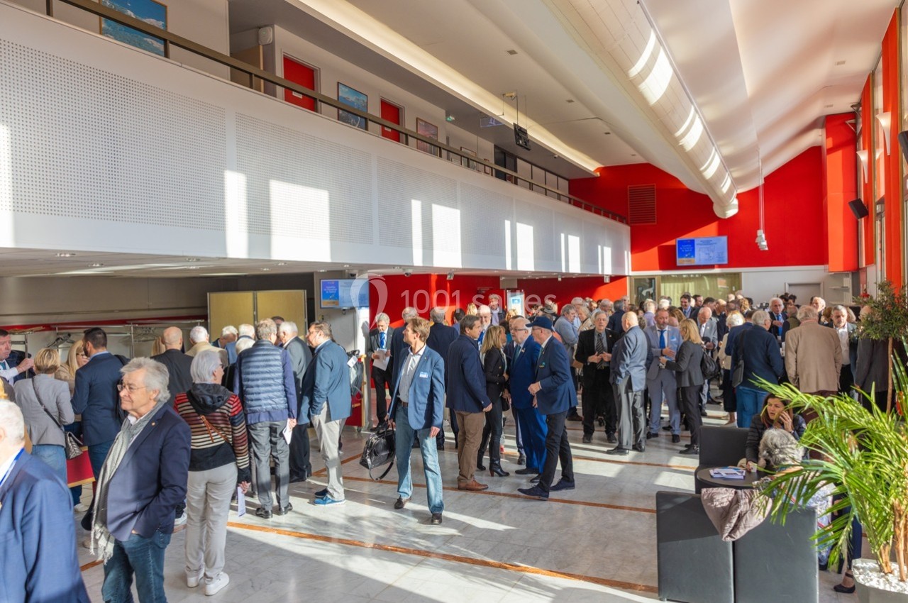 Groupe de personnes rassemblées dans un hall lumineux avec des murs rouges et blancs, discutant debout.