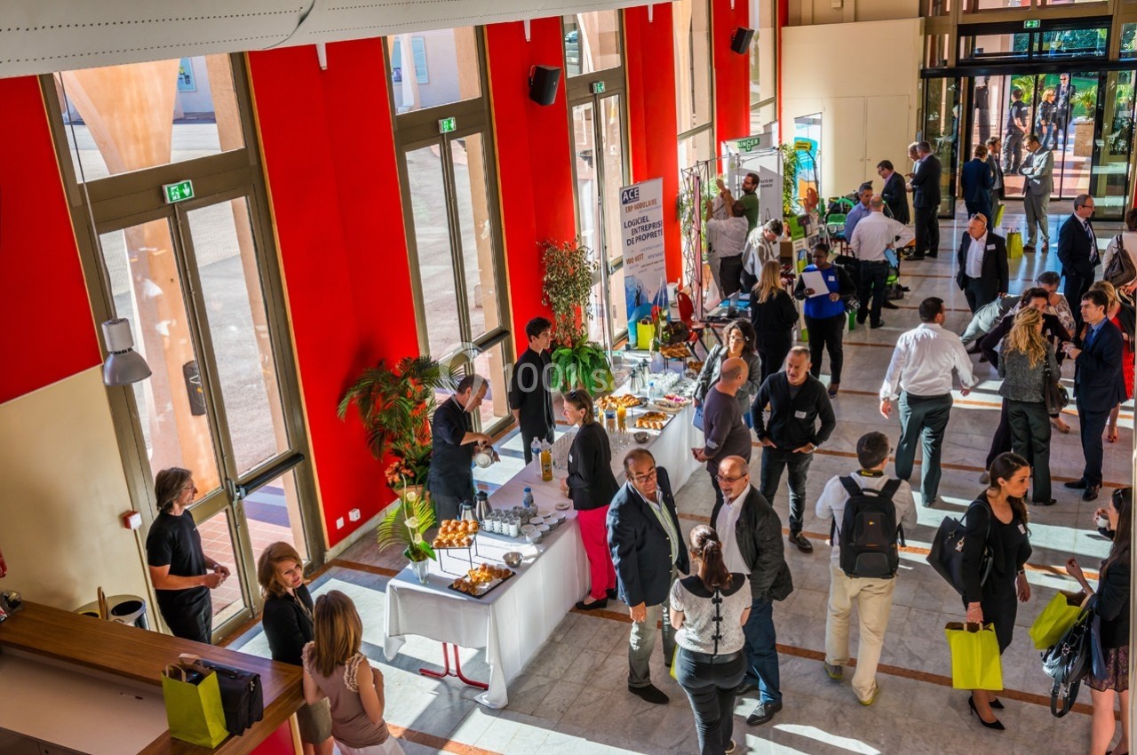 Des personnes discutent et se déplacent dans un hall lumineux lors d'un événement avec des stands et des tables de…
