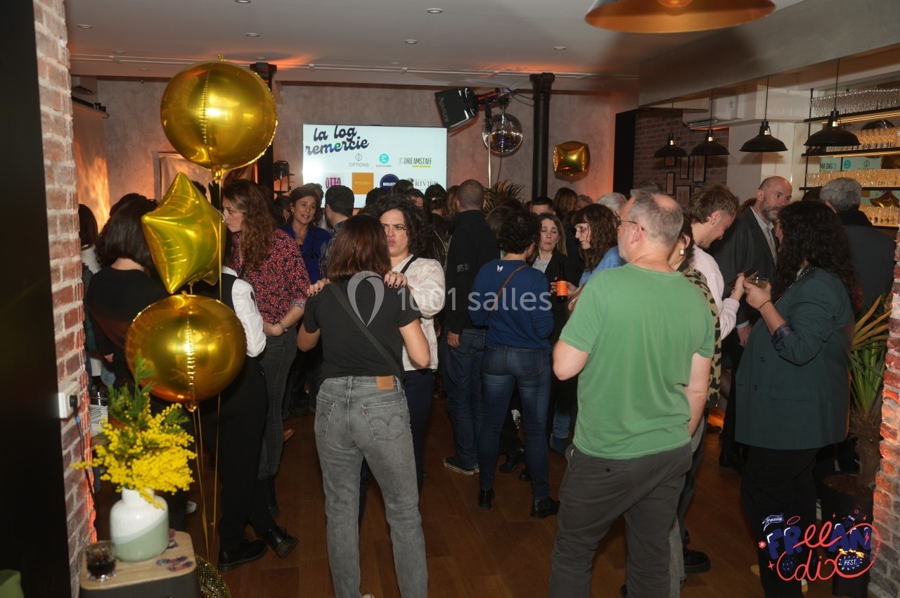 Groupe de personnes rassemblées dans une salle décorée avec des ballons dorés et un écran projetant un visuel.