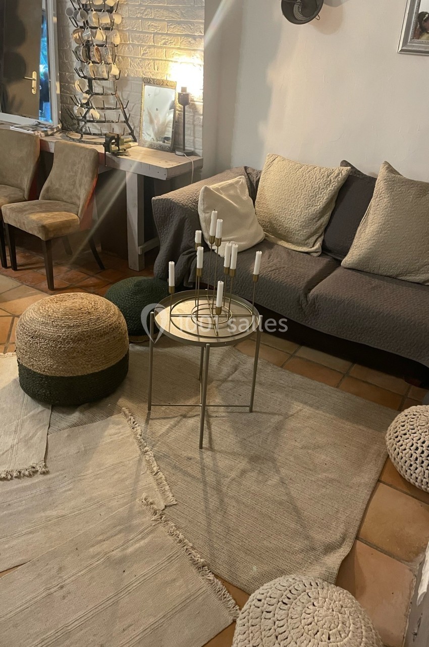 Salon cosy avec canapé gris, poufs en osier, tapis clairs et table basse ronde avec bougeoirs.
