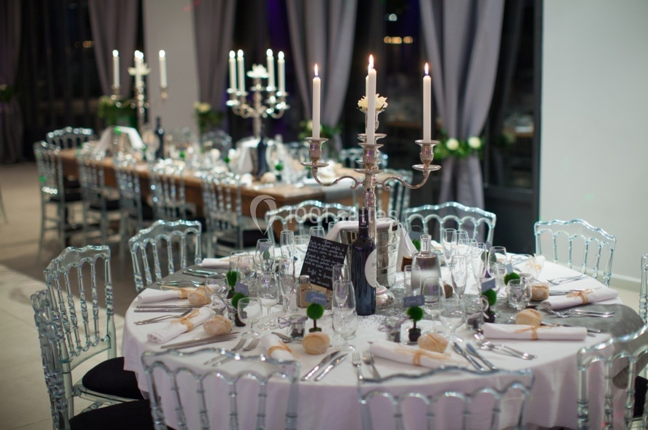 Table élégamment dressée avec chandeliers, vaisselle raffinée et décorations, dans une salle de réception lumineuse.