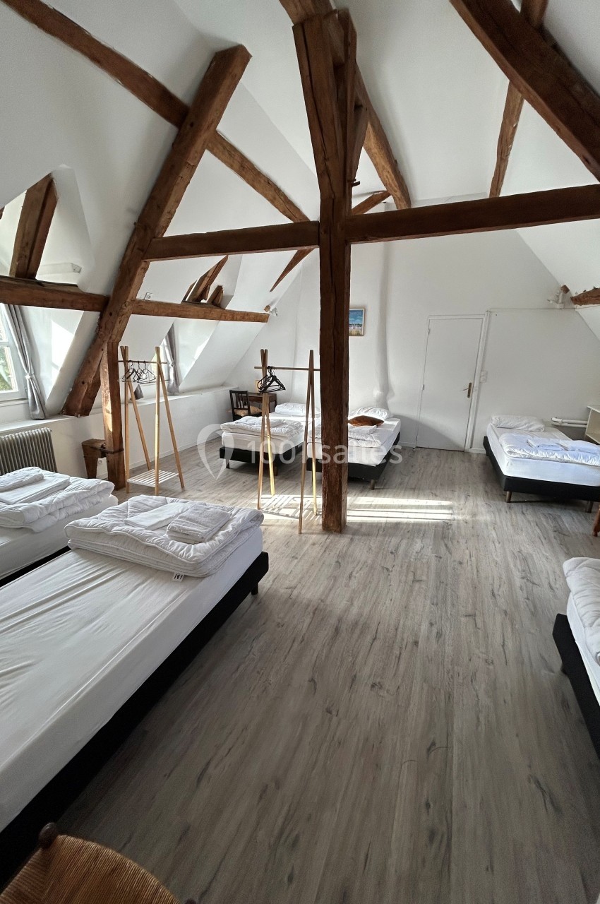 Chambre spacieuse sous combles avec poutres apparentes, lits simples alignés et parquet clair.