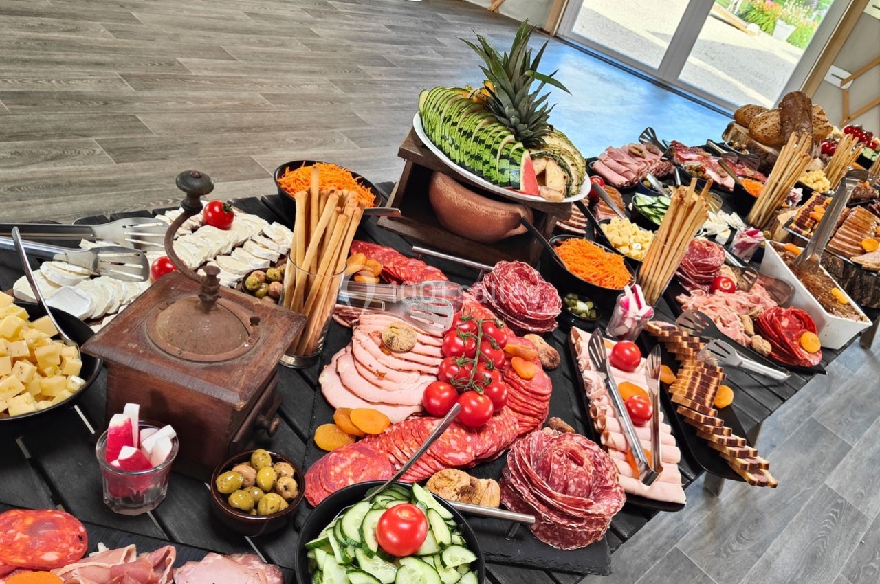 Buffet varié avec charcuteries, fromages, légumes frais, pains et fruits, présenté sur une table en bois.