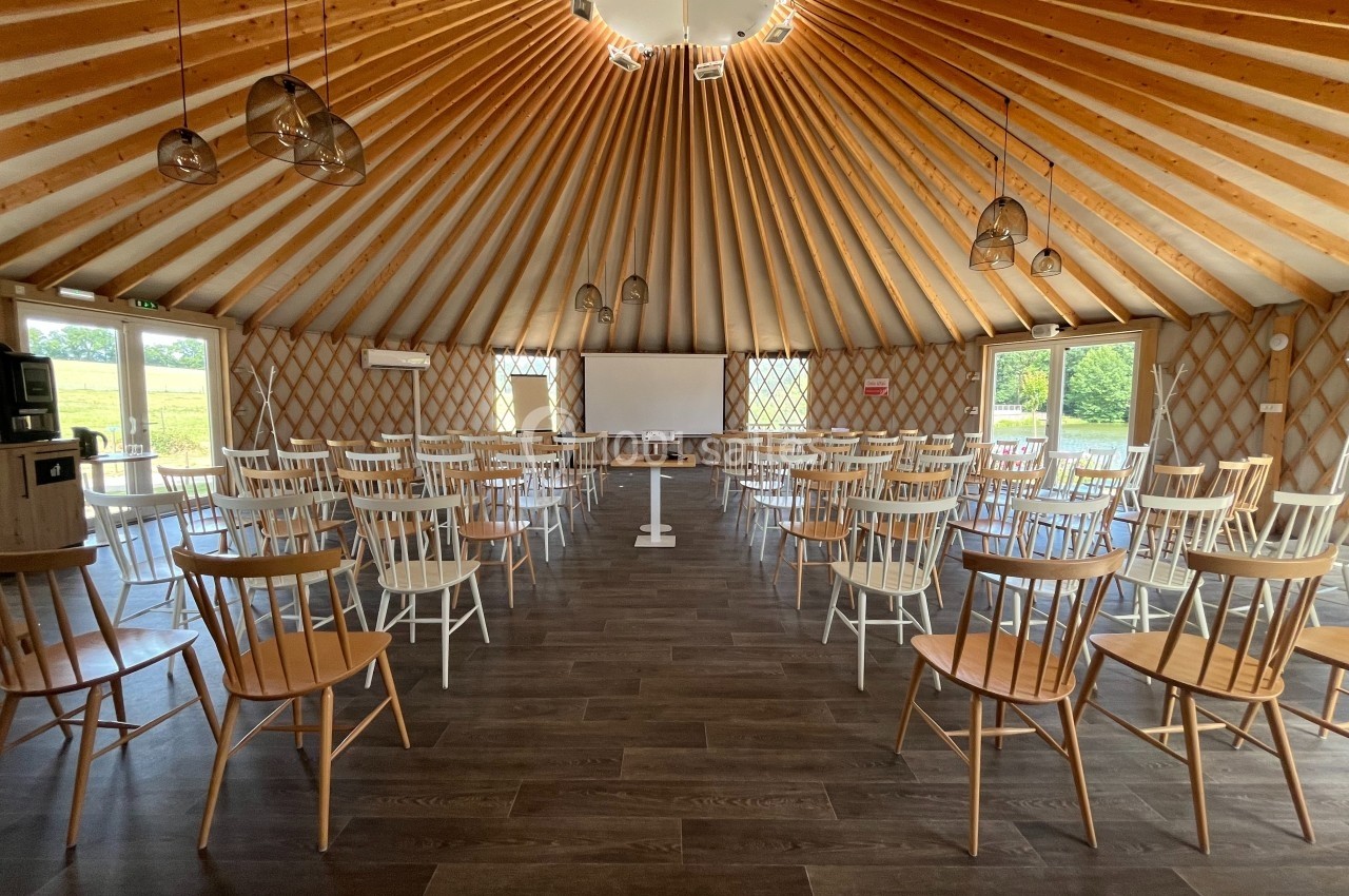 Salle circulaire en bois avec des rangées de chaises disposées face à un écran de projection et un tableau blanc.