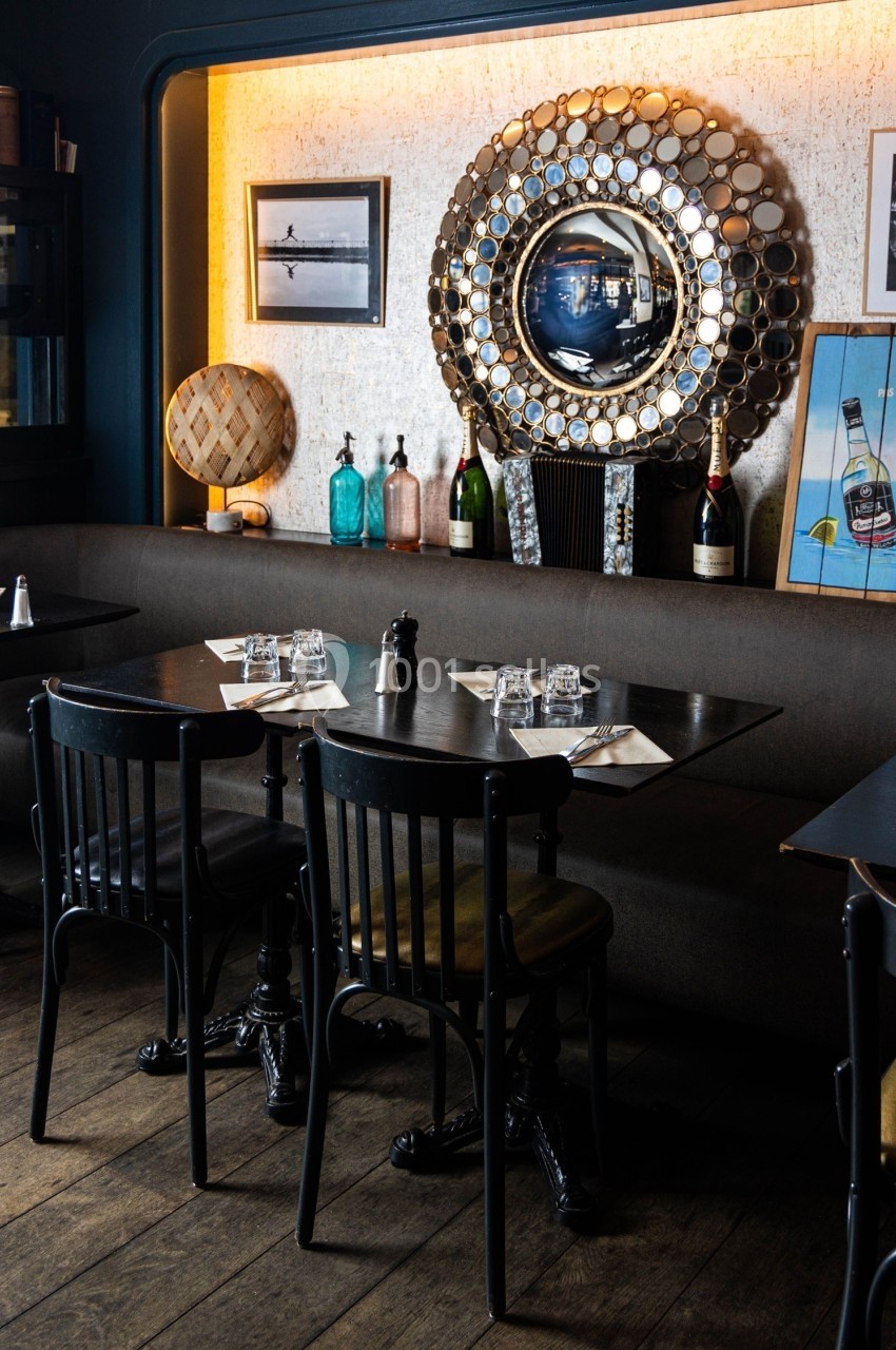 Salle de restaurant avec tables en bois, chaises noires, décorations murales et bouteilles exposées.