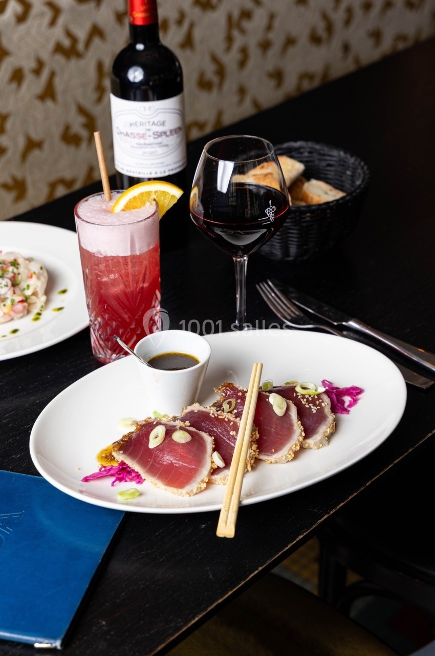 Assiette de thon mi-cuit avec sauce, accompagnée d'un cocktail, d'un verre de vin rouge et d'un panier de pain.