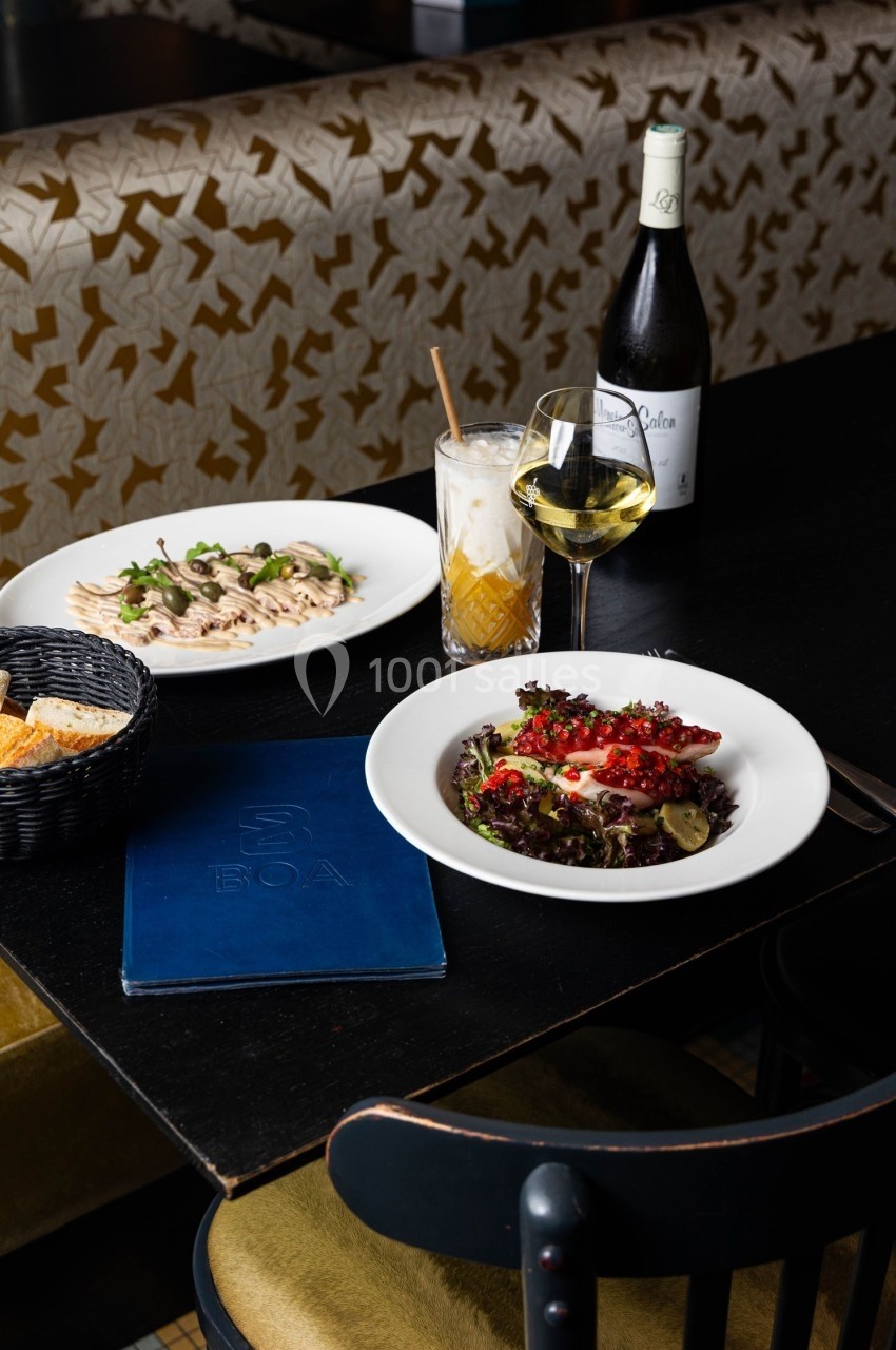 Table de restaurant avec des plats servis : poulpe grillé, pâtes, pain, accompagnés de vin blanc et d'un cocktail.