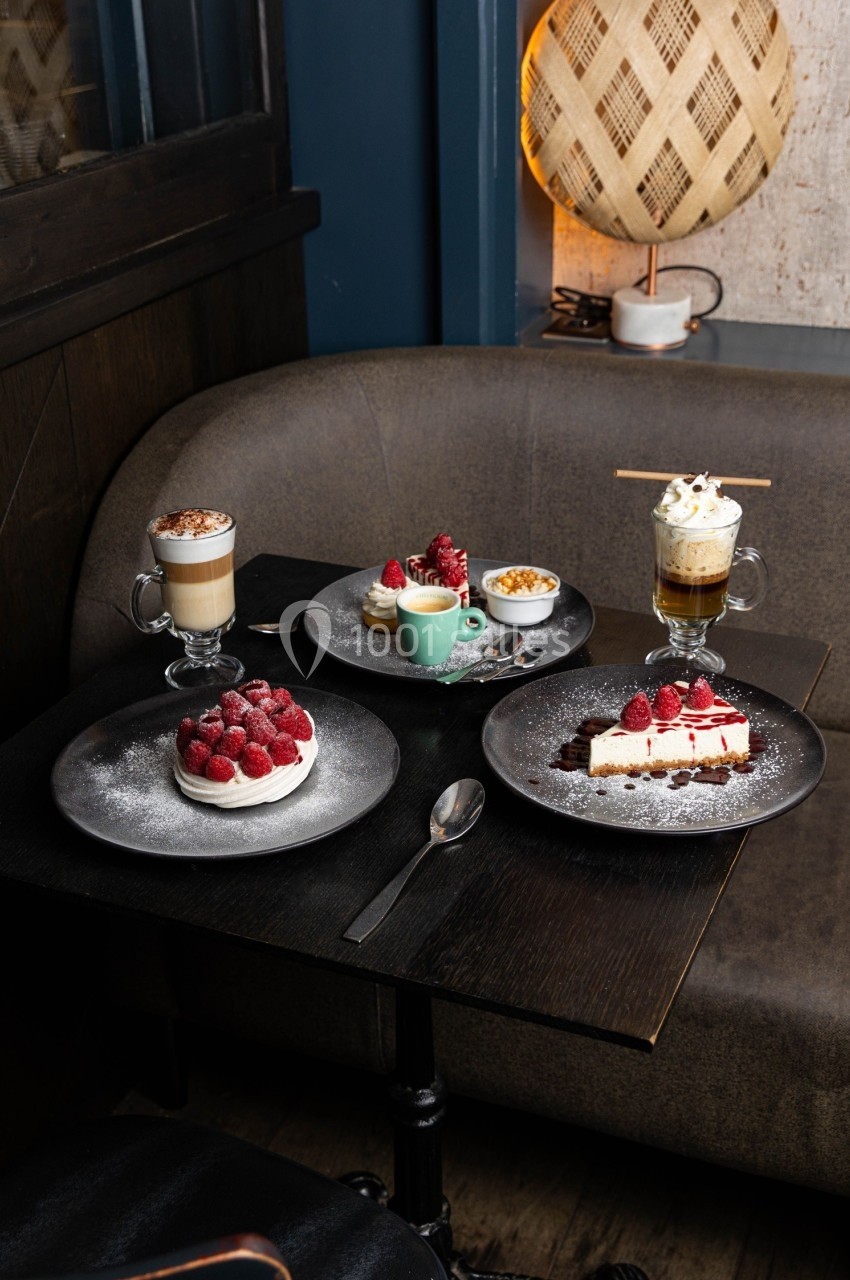 Desserts variés avec des fruits rouges, boissons chaudes et décor rustique sur une table sombre dans un café.