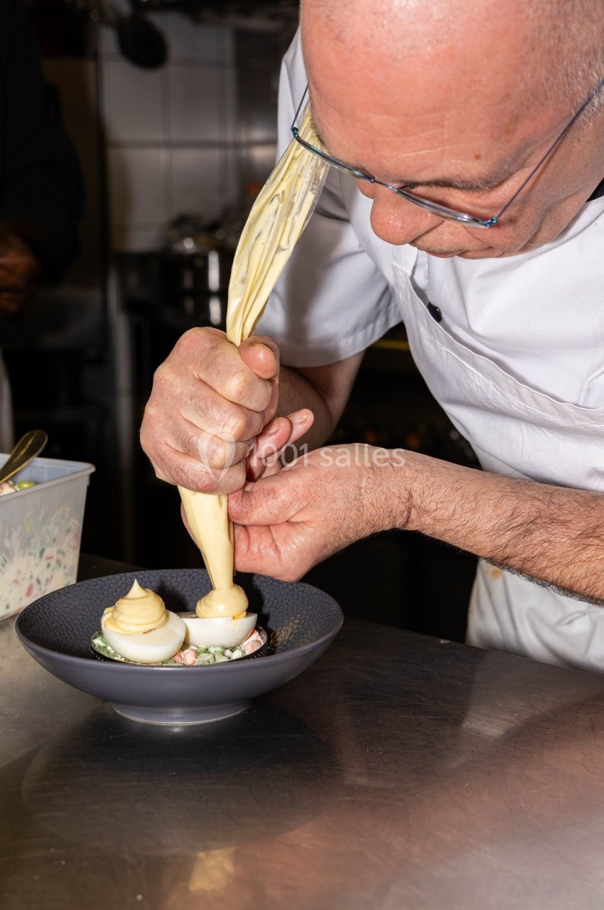 Un chef en train de dresser une assiette avec une poche à douille dans une cuisine professionnelle.