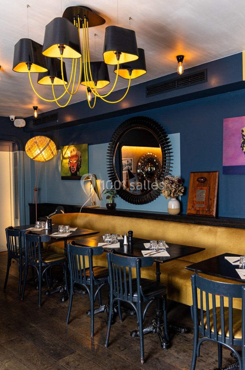 Salle de restaurant avec tables en bois noir, banquette jaune, décoration murale et lustre moderne noir et jaune.