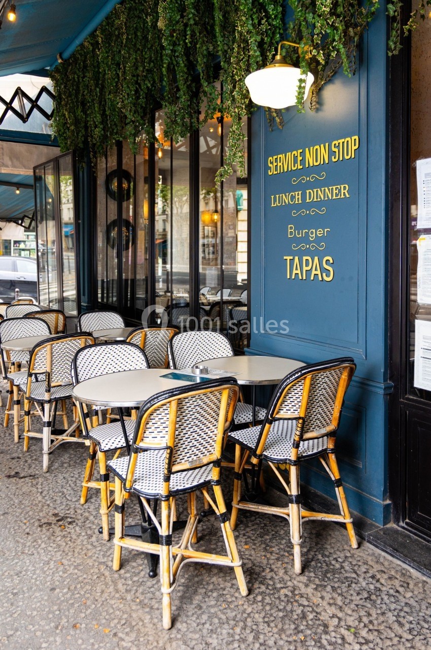 Terrasse d'un café-restaurant avec des tables et chaises en osier, devanture bleue et enseigne mentionnant le service…