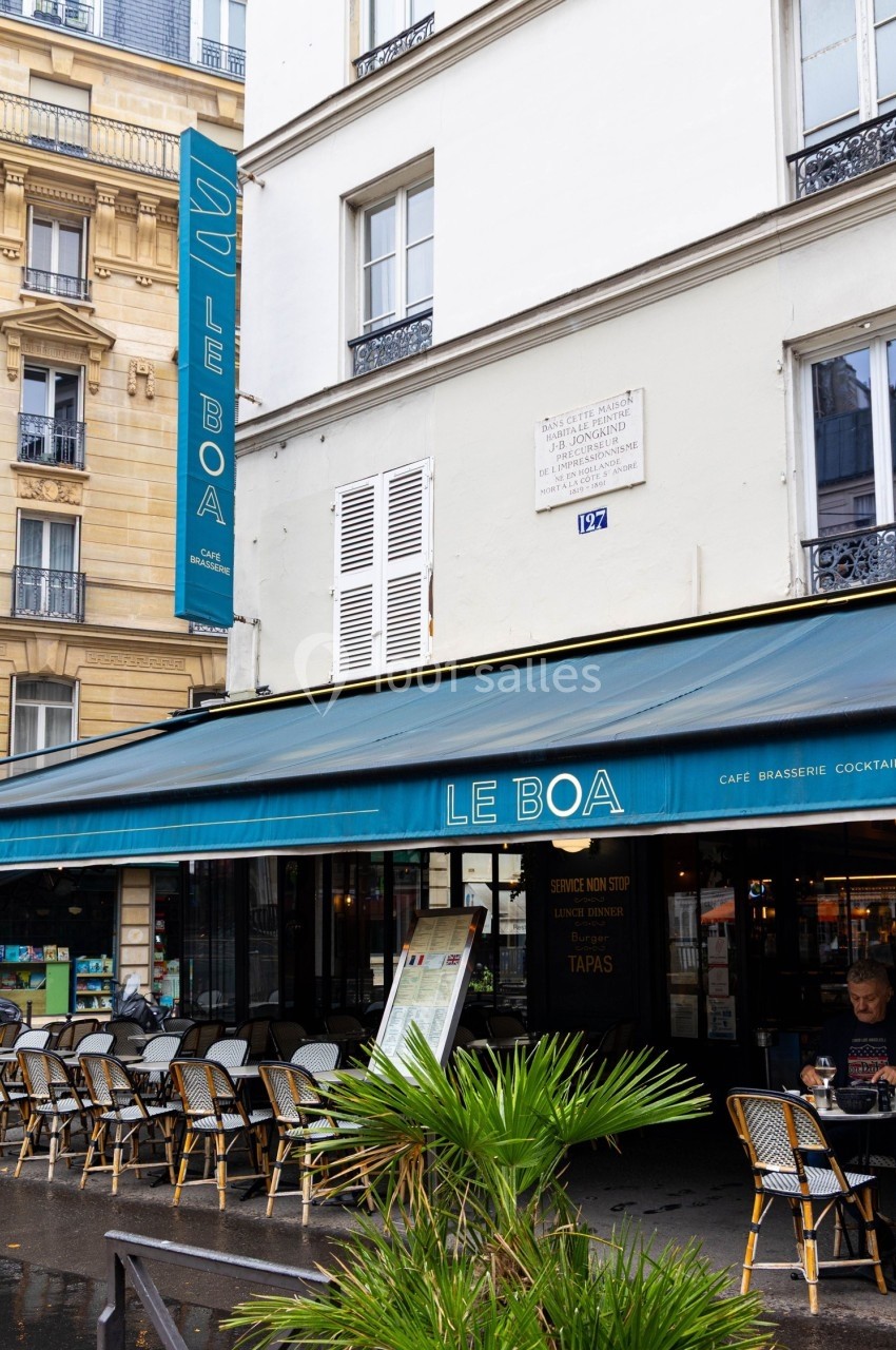 Façade d'un café parisien avec terrasse extérieure, auvent bleu et enseigne verticale indiquant ’Le Boa’.