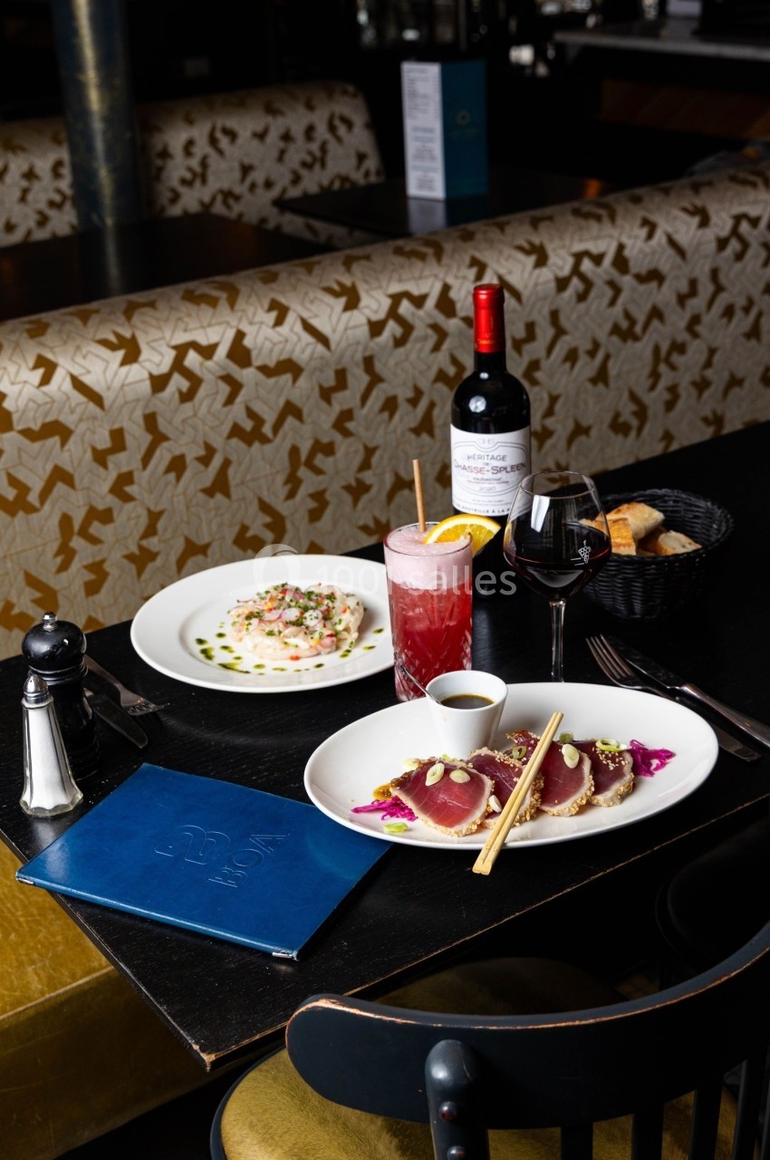 Table de restaurant avec un plat de thon, un cocktail, un verre de vin, une bouteille de vin et un panier de pain.
