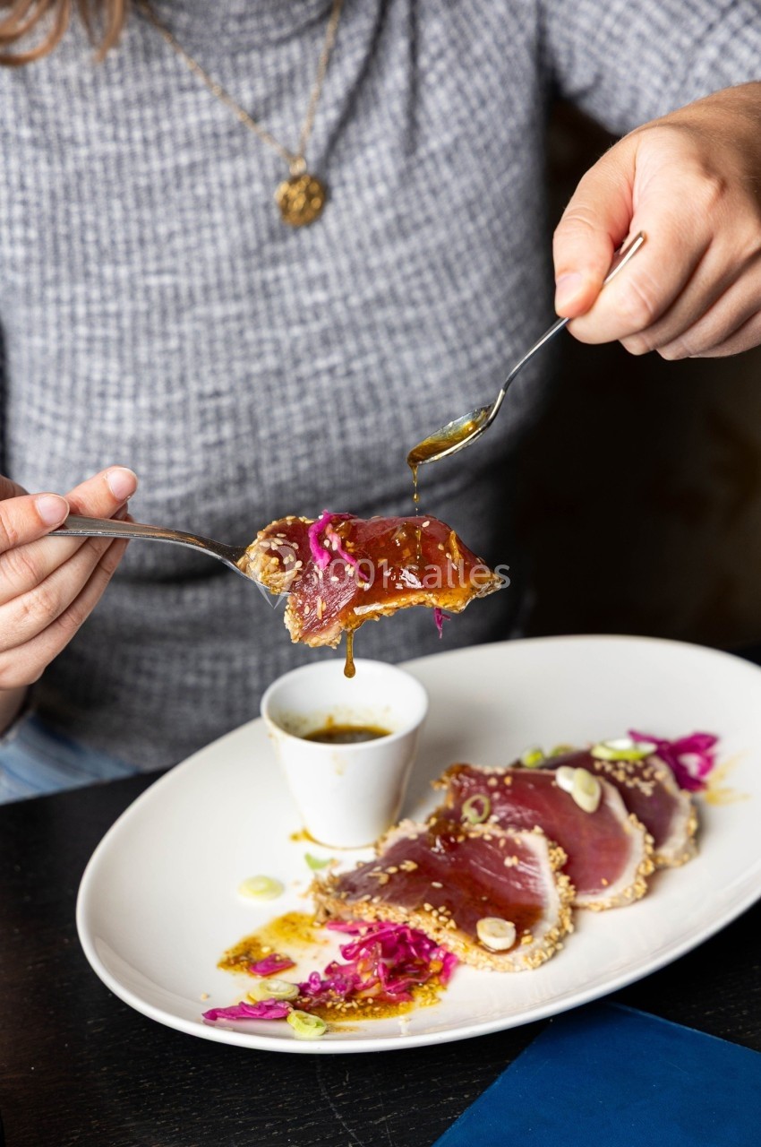 Une personne tient une tranche de thon mi-cuit avec une fourchette au-dessus d'une assiette garnie et d'une sauce.