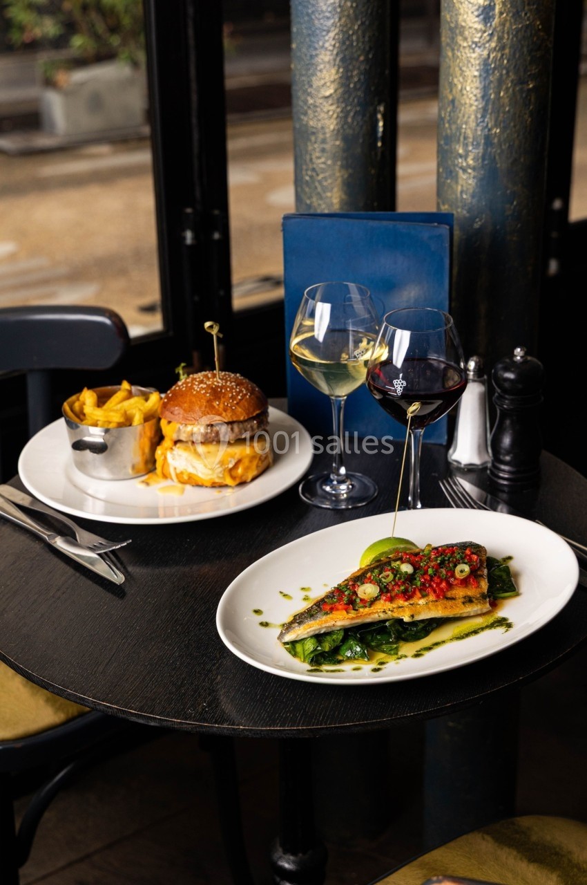 Repas composé d'un burger avec frites et d'un plat de poisson grillé, servi sur une table dans un restaurant.