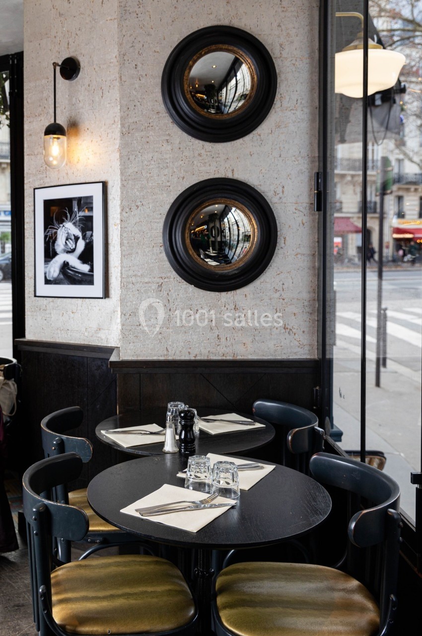Tables rondes noires avec chaises, miroirs circulaires et photo encadrée sur un mur clair dans un café parisien.