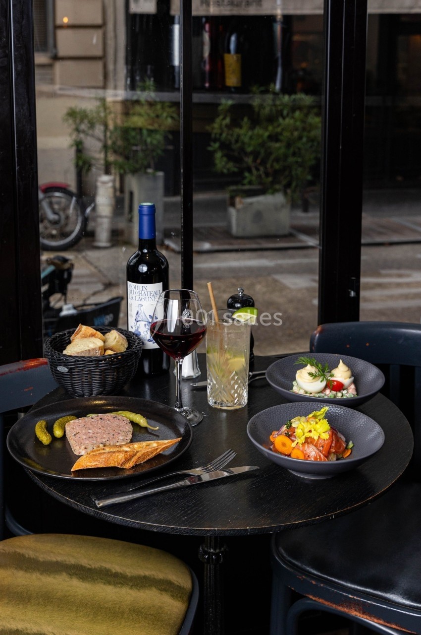 Table de restaurant avec assiettes de charcuterie, légumes, pain, cornichons, verre de vin rouge et bouteille de vin.
