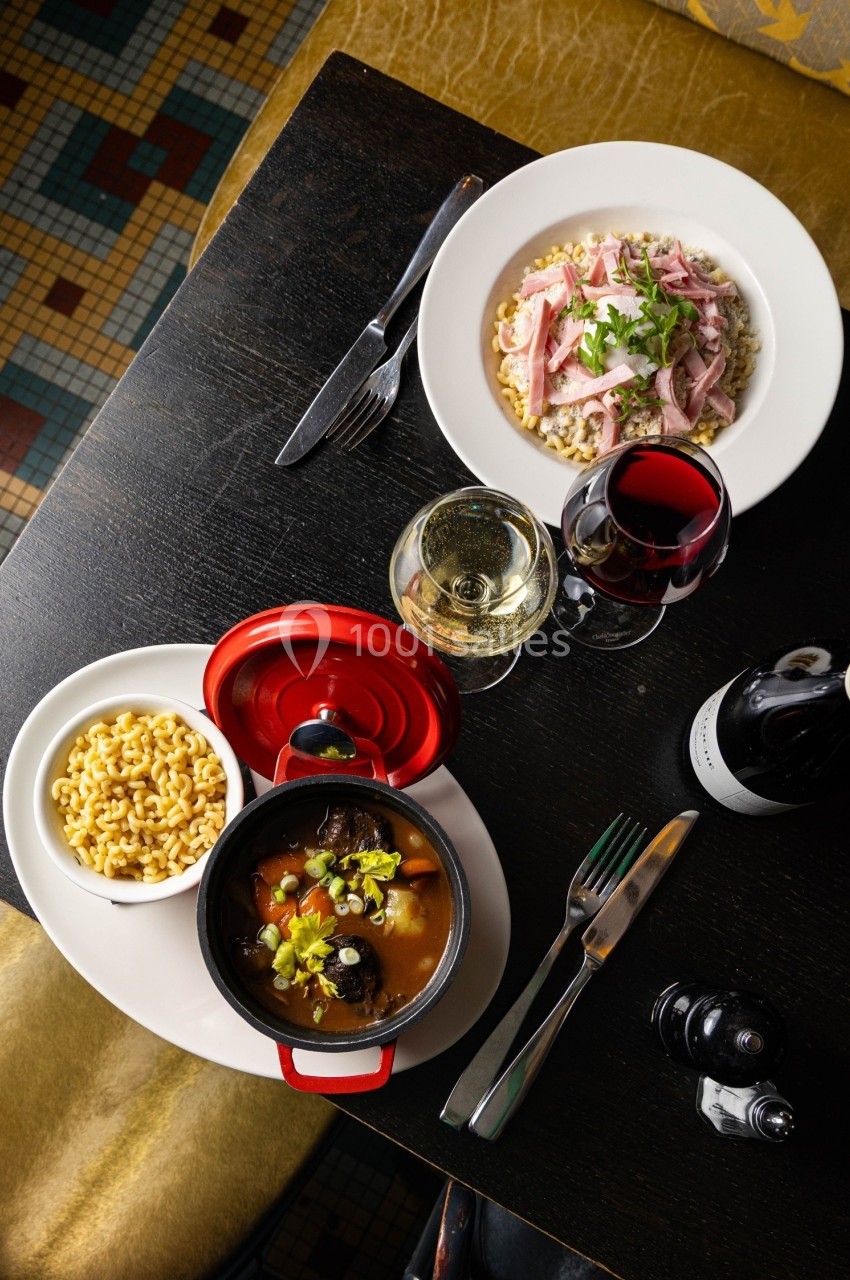 Vue de dessus d'une table avec un plat mijoté, des pâtes, une assiette de viande, deux verres de vin et des couverts.