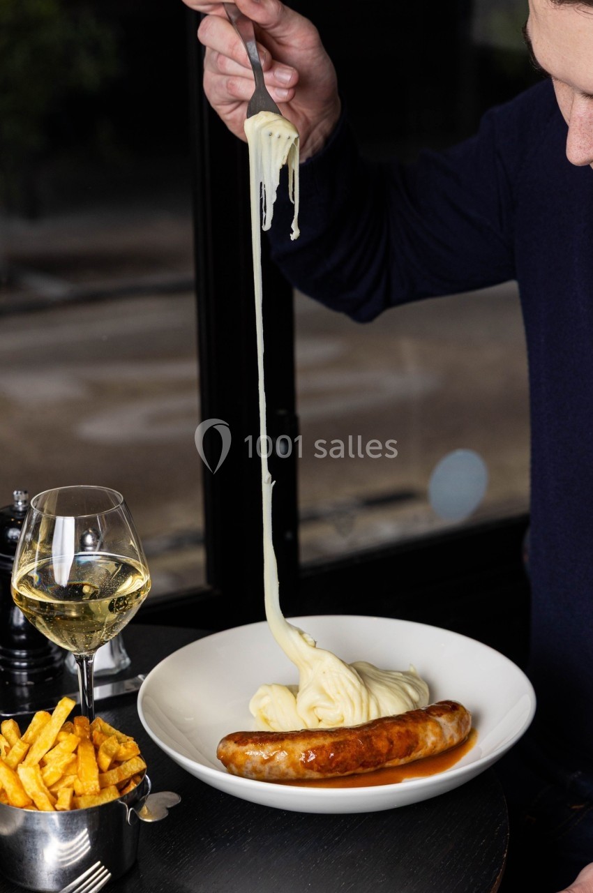Une assiette avec une saucisse, de la purée filante, accompagnée de frites et d'un verre de vin blanc.