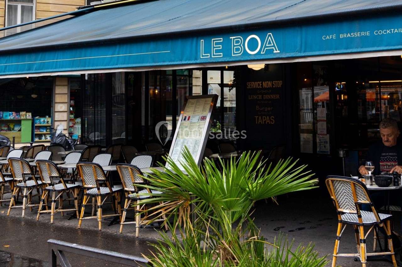 Terrasse d'un café-restaurant avec chaises en osier, devanture bleue et menu affiché sous un auvent.