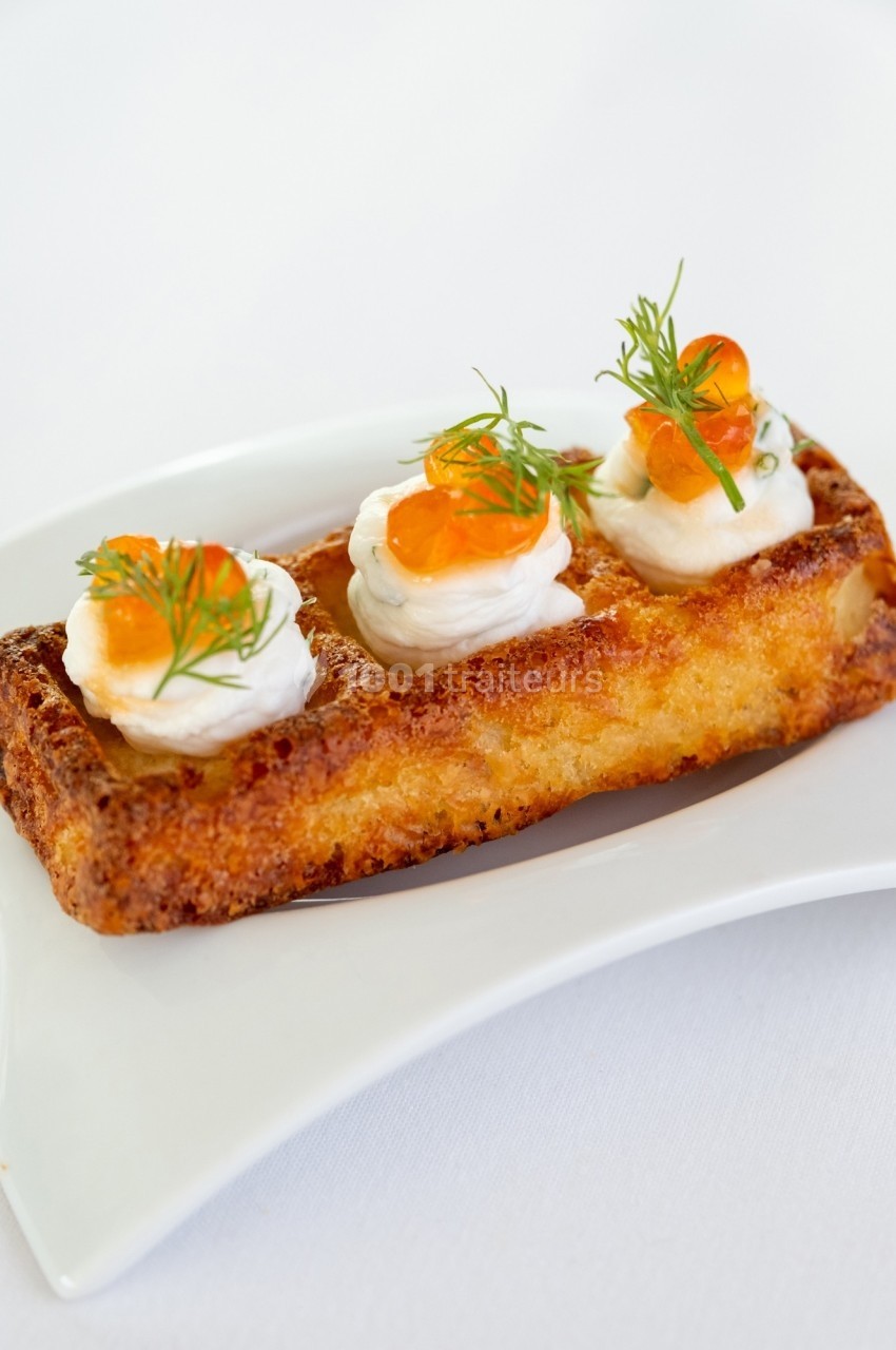 Gaufre croustillante garnie de crème, œufs de poisson orange et brins d'aneth, servie sur une assiette blanche.