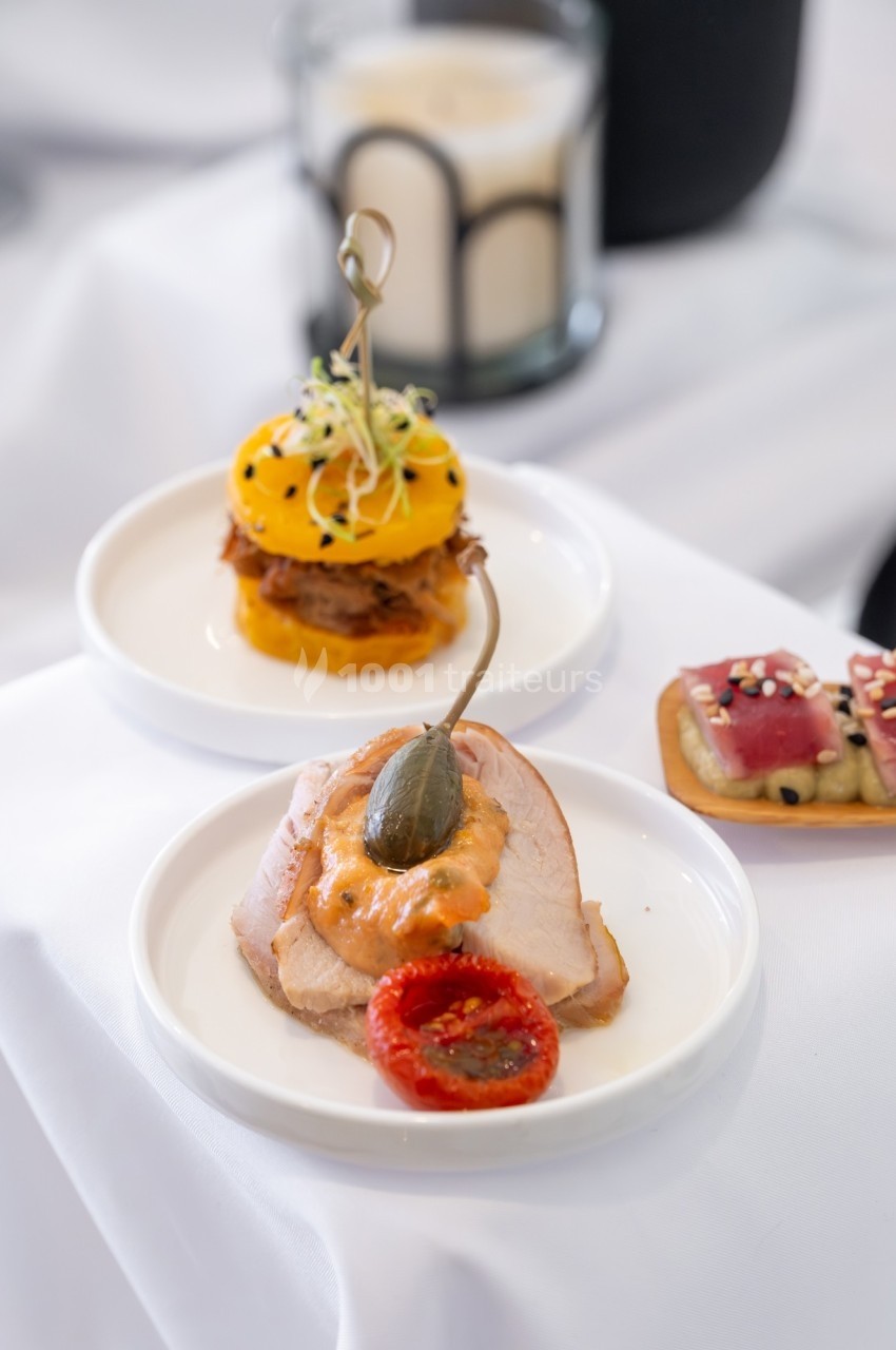 Assiette de bouchées gastronomiques comprenant viande, légumes et garnitures, présentées sur une nappe blanche.
