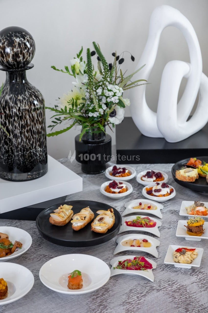 Table dressée avec des amuse-bouches variés, accompagnée de décorations modernes et d'un bouquet de fleurs blanches.