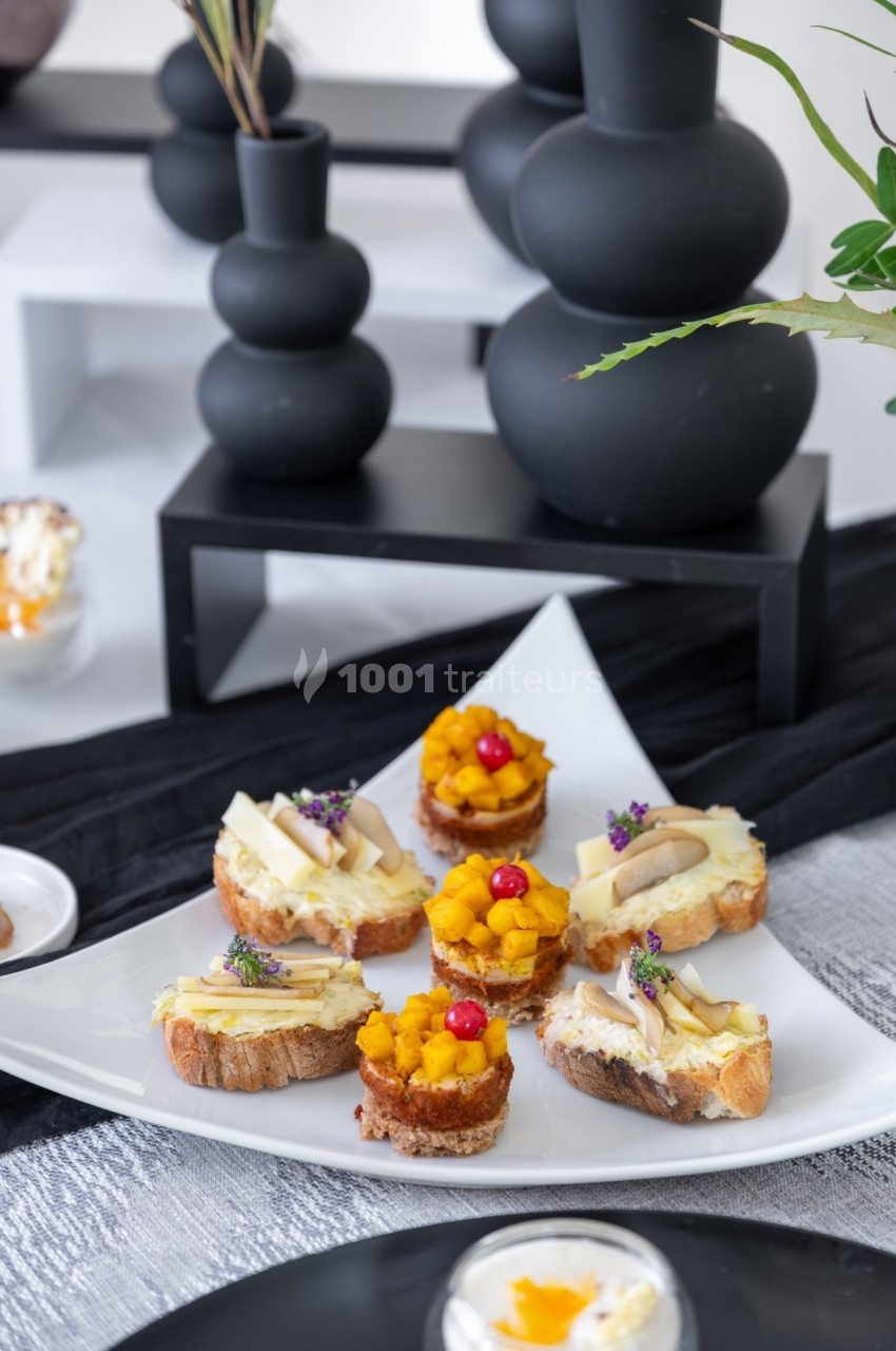 Assortiment de toasts garnis de fromage, purée et baies rouges, présenté sur une assiette blanche.