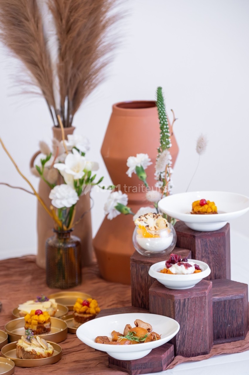 Présentation artistique de plats gastronomiques sur des supports en bois, avec une décoration florale en arrière-plan.