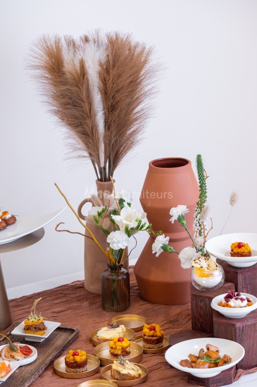 Assortiment de desserts et décorations florales sur une table avec vases en céramique et herbes séchées.