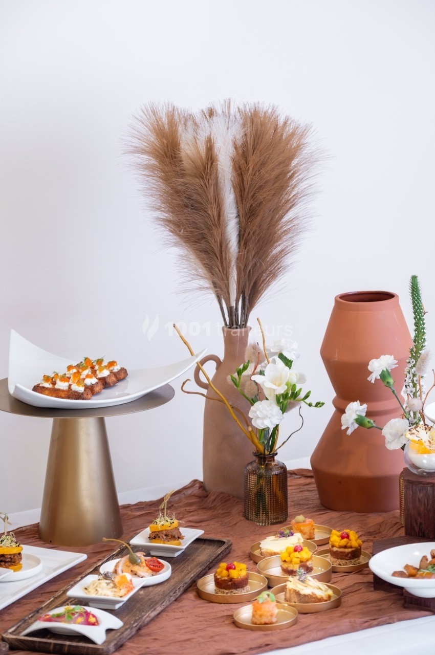 Table décorée avec des vases en céramique, des fleurs séchées et des assiettes contenant des amuse-bouches variés.
