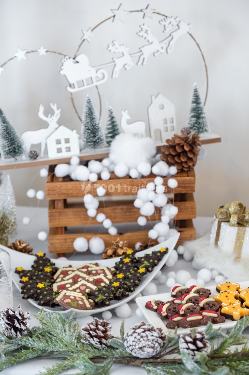 Plateau de biscuits de Noël décorés entouré de décorations festives, sapins miniatures et guirlandes.