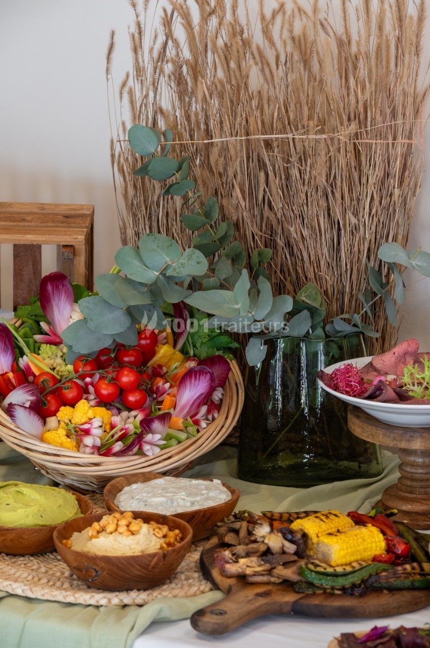 Assortiment de légumes colorés, sauces et épis de maïs grillés disposés sur une table avec des herbes sèches en arrière-plan.