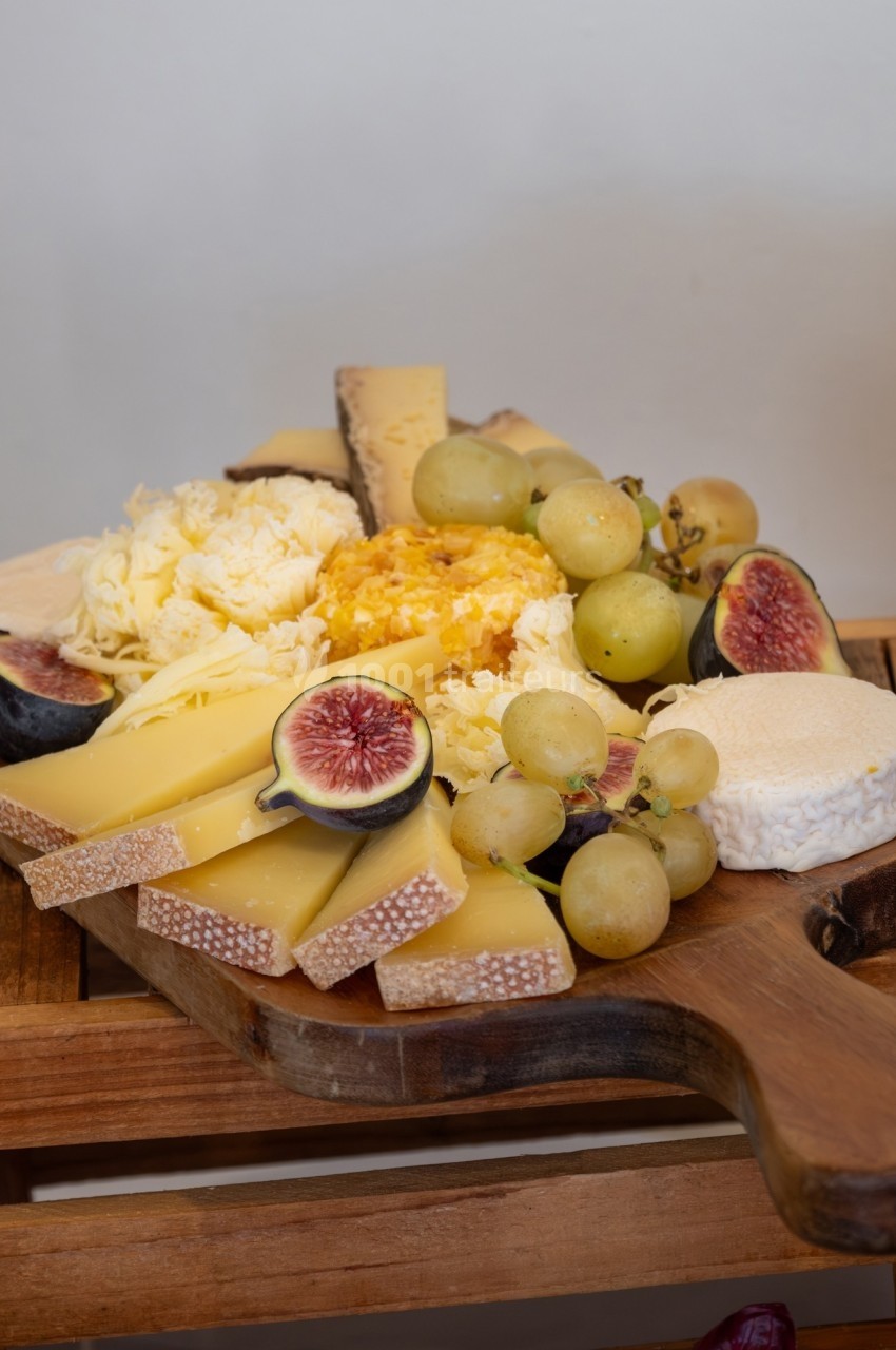 Plateau de fromages variés accompagné de raisins, figues fraîches et miel, présenté sur une planche en bois.
