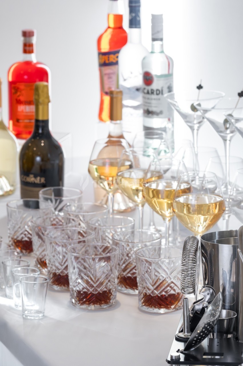 Verres de cocktails remplis et bouteilles d'alcool variées disposés sur une table blanche éclairée.