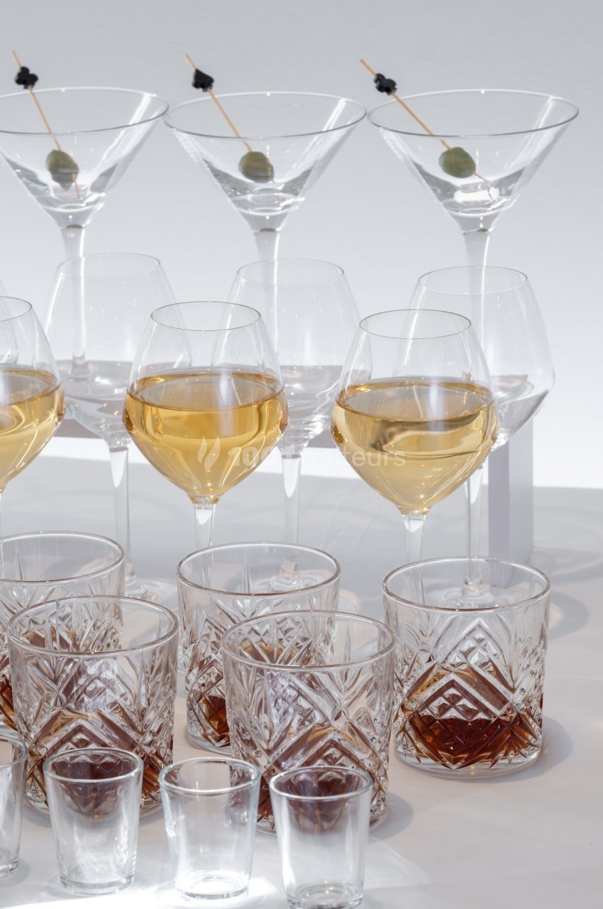 Verres de différentes formes contenant des boissons variées, disposés sur une surface blanche.