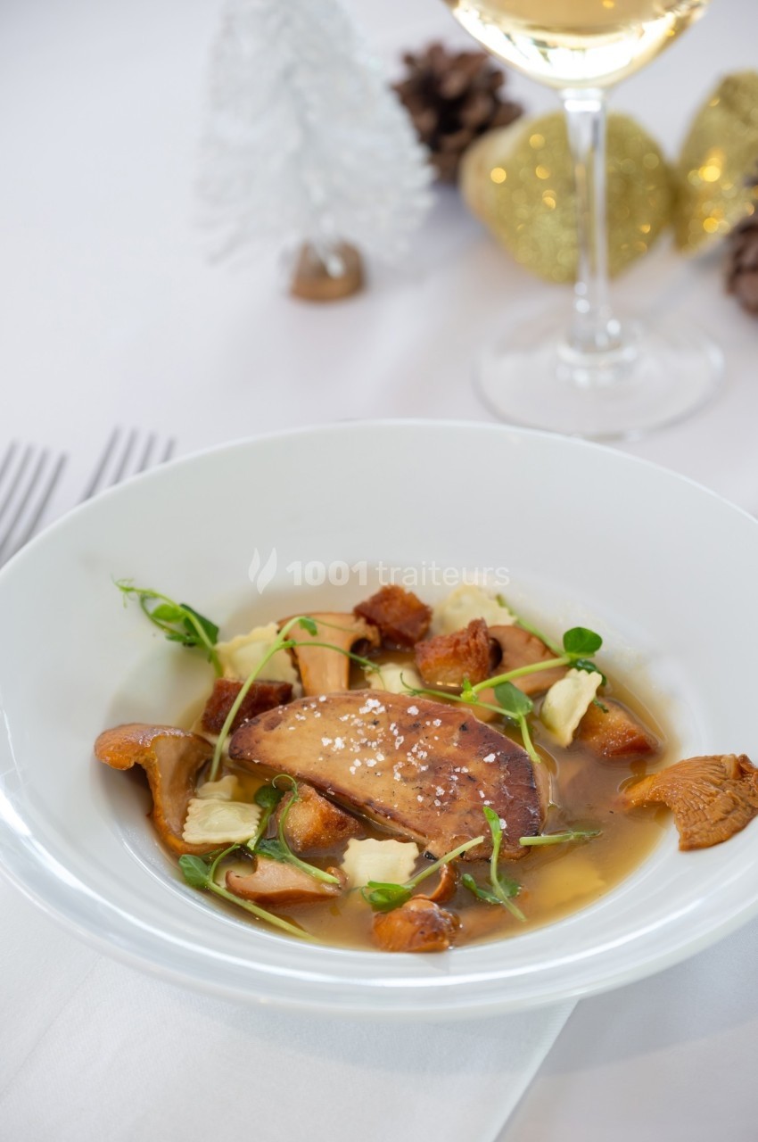Assiette de foie gras poêlé avec champignons, herbes fraîches et bouillon, servie sur une table décorée pour les fêtes.
