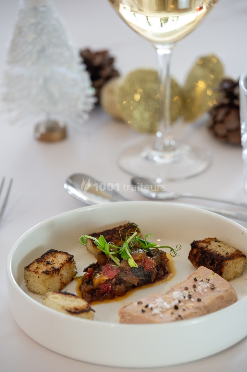 Assiette gastronomique avec foie gras, pain grillé et garniture, sur une table décorée pour les fêtes.