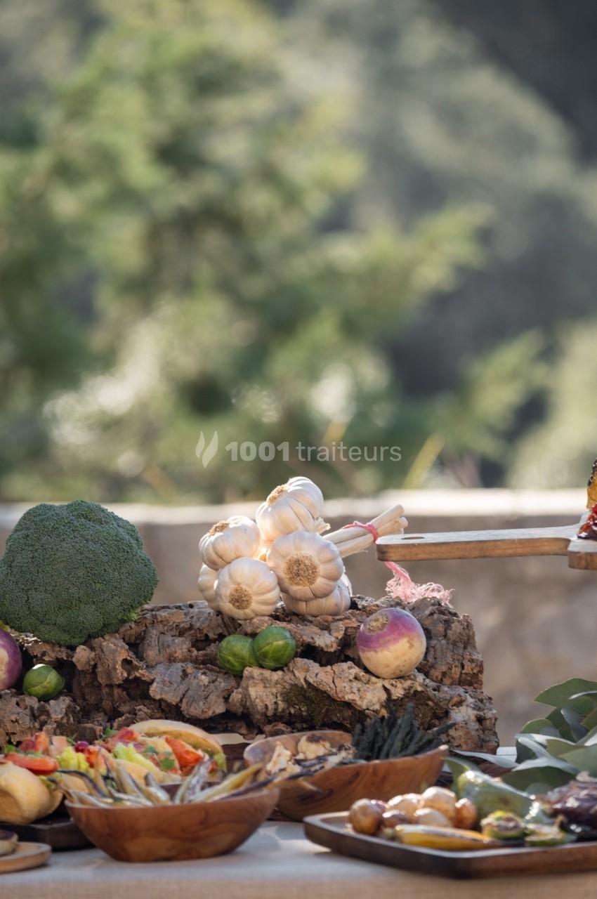 Légumes frais, fruits et plats disposés sur une table en extérieur, avec un fond naturel flou.