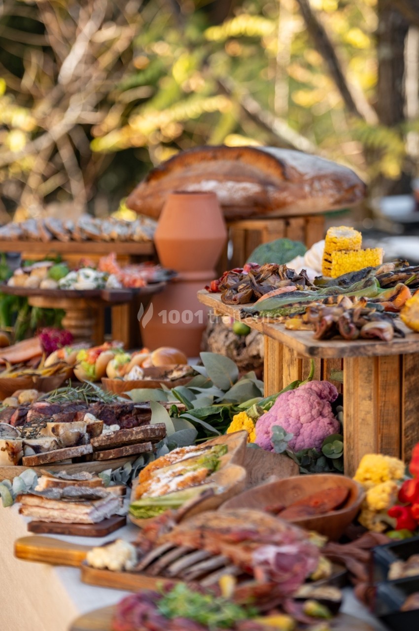 Buffet en plein air avec une variété de plats, légumes colorés, pains, et charcuteries disposés sur des plateaux en bois.
