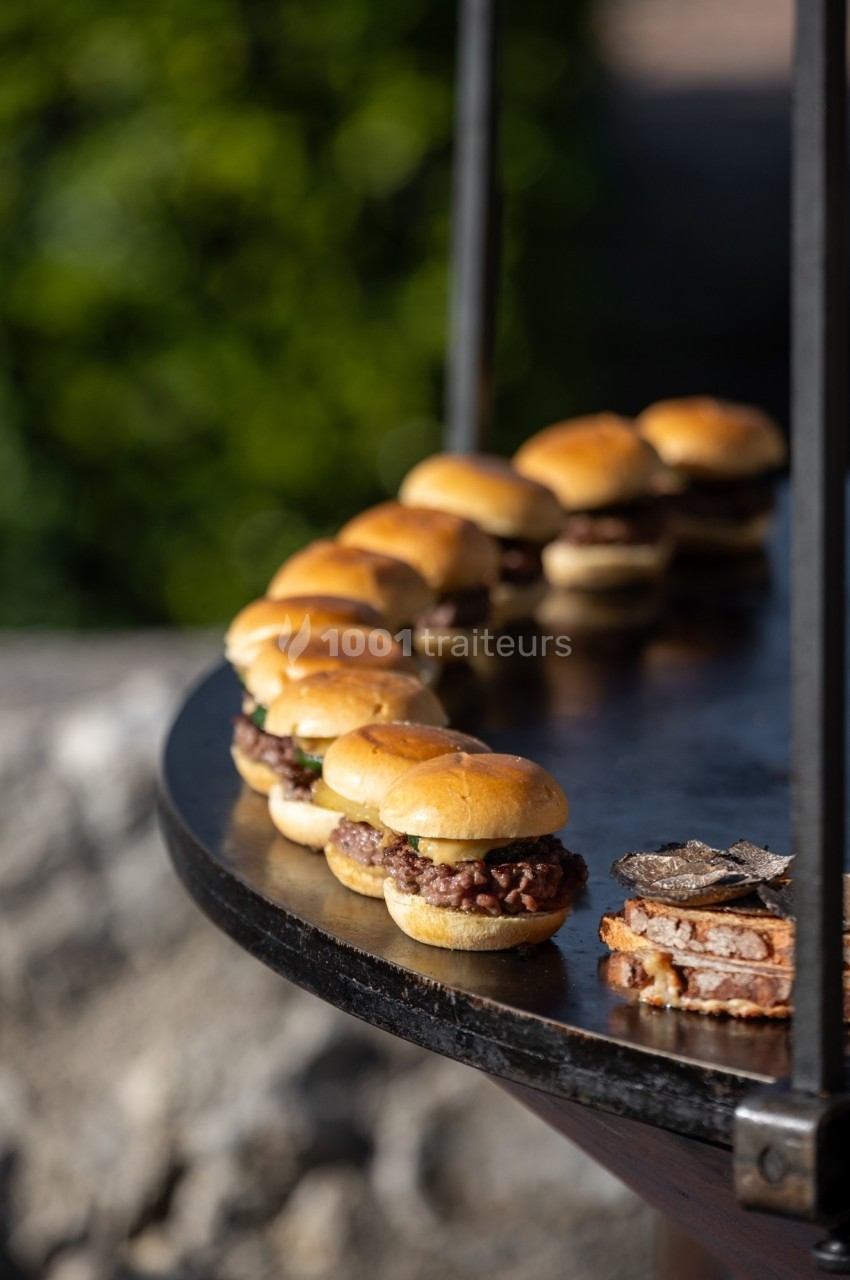 Mini-burgers alignés sur une table ronde en extérieur, avec des tranches de pain garnies de truffes au premier plan.