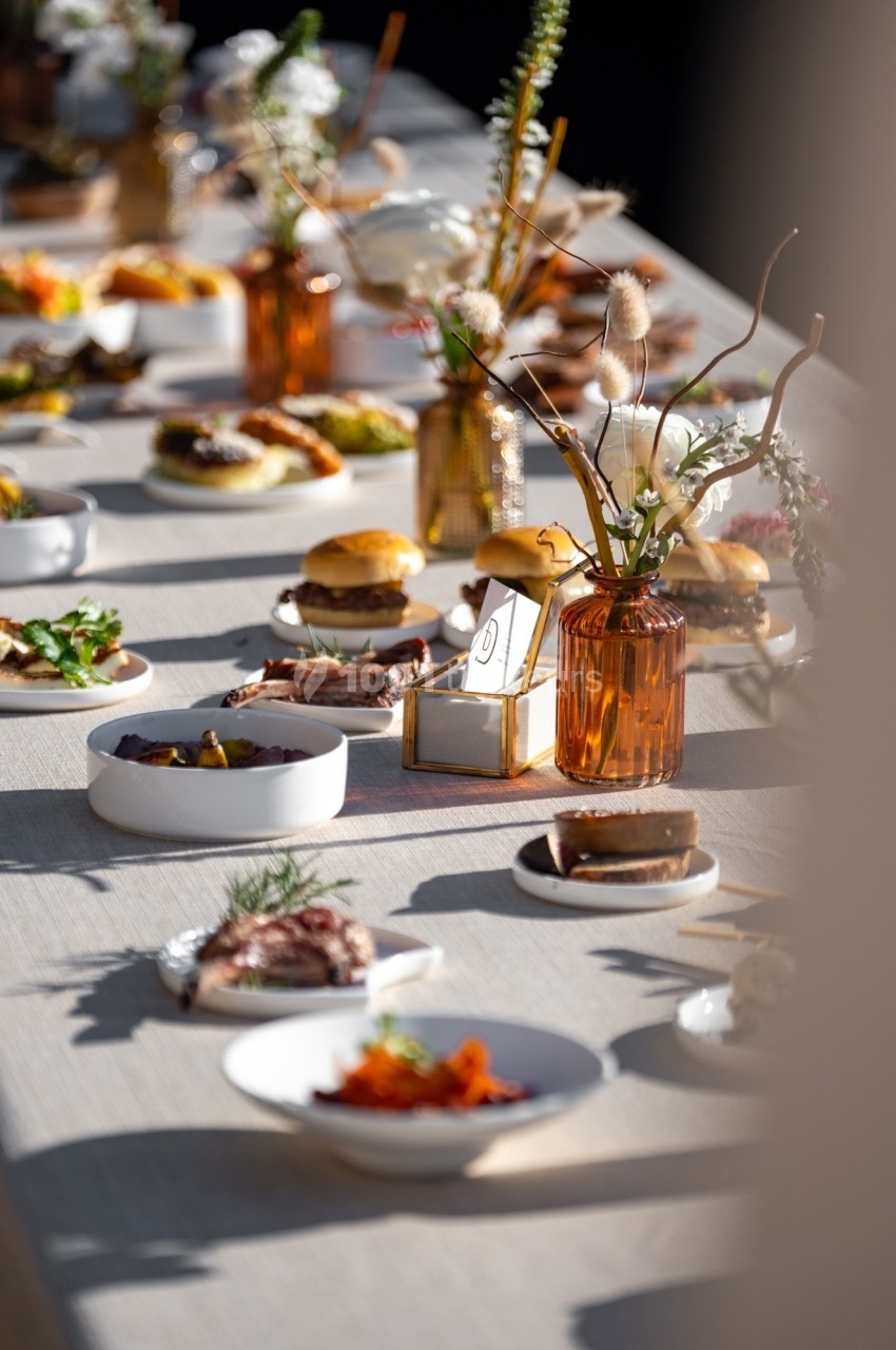 Table dressée avec divers plats, fleurs en vase ambré et lumière naturelle créant une ambiance chaleureuse.